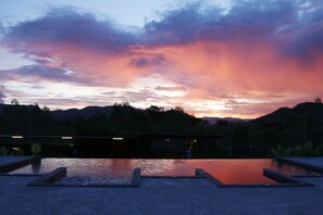 Une piscine avec vue sur le coucher de soleil, entourée d’un espace paysager et avec un bâtiment en arrière-plan.