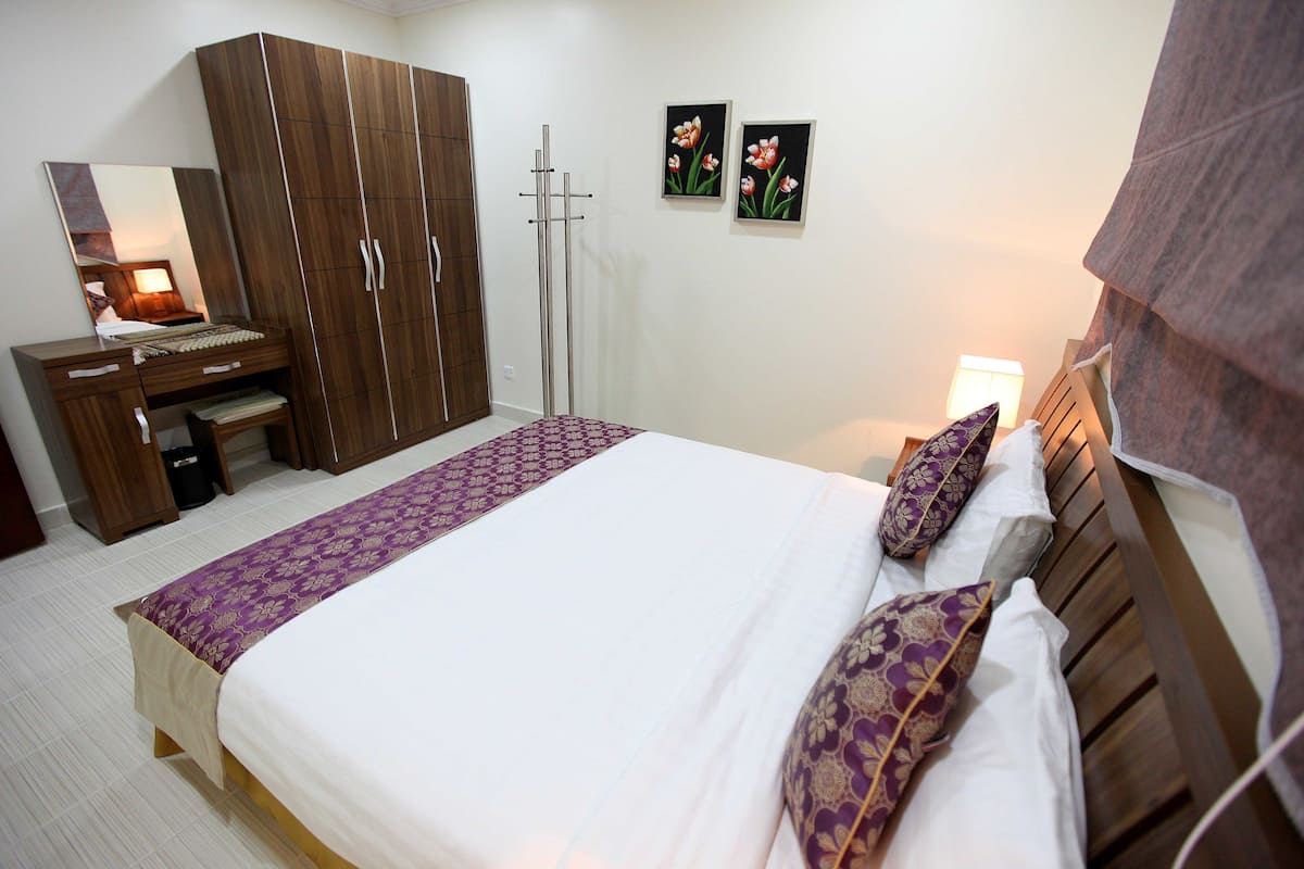 A bedroom with a bed, wooden wardrobe, bedside table, and a mirror.