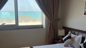 Une chambre d’hôtel avec un grand lit, une table de chevet, une lampe et une vue sur la plage.