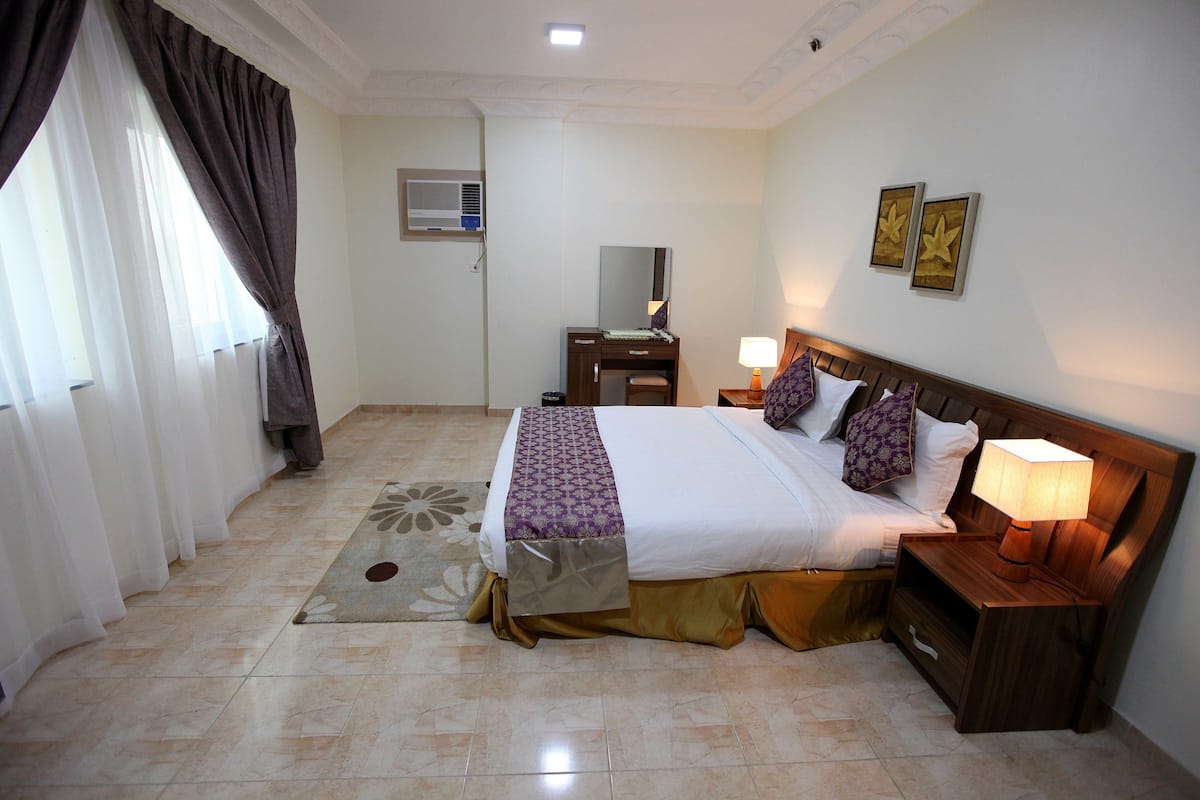 A hotel room with a bed, nightstands, a desk, and a window with curtains.