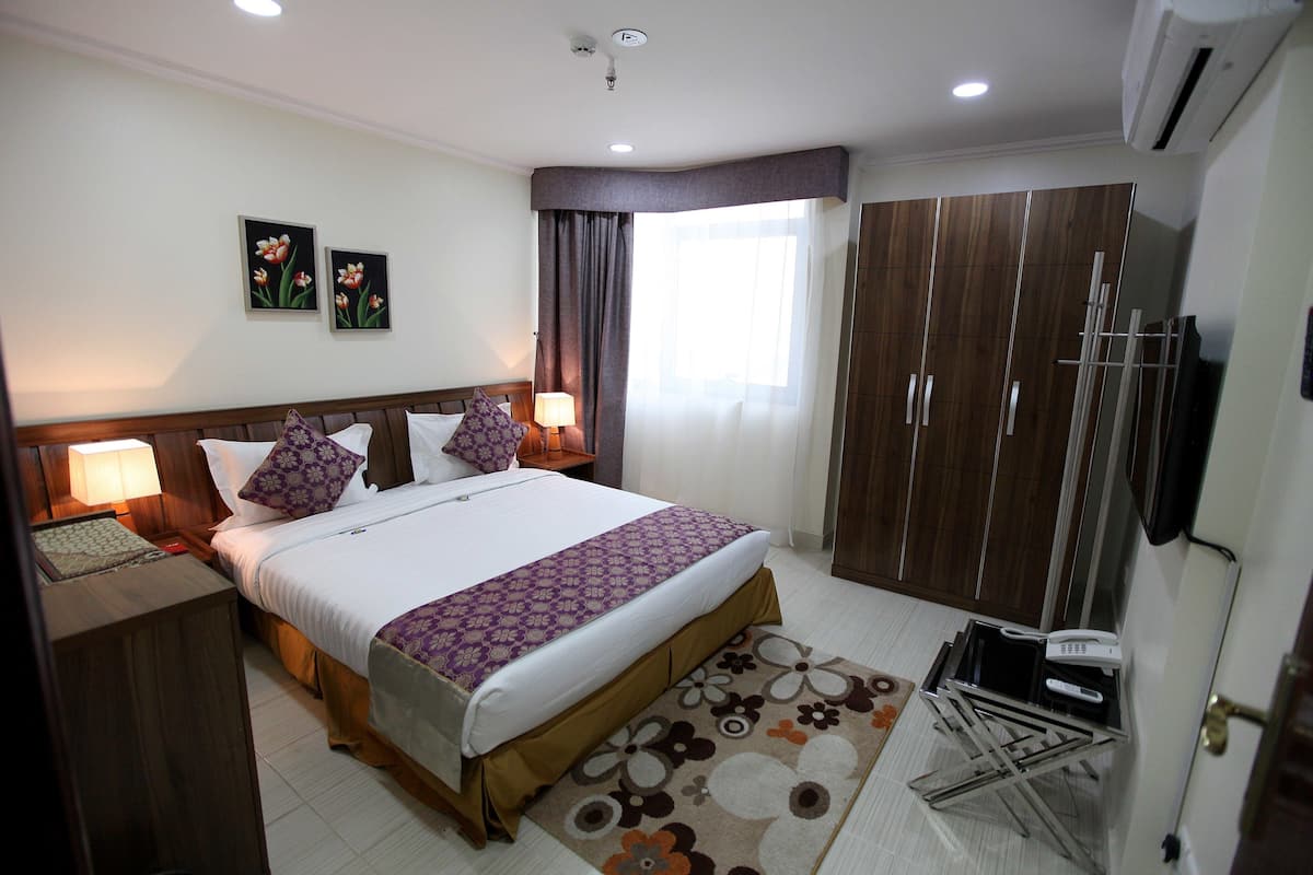 A hotel room with a bed, bedside tables, a wardrobe, a TV, and a window with curtains.