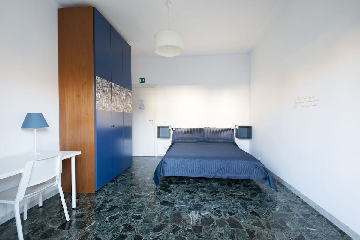 A bedroom with a bed, a desk, a lamp, and a wardrobe.