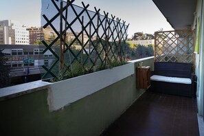 Un balcon avec une balustrade en treillis, un banc en osier et une vue sur les bâtiments en arrière-plan.