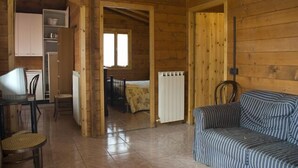 A wooden cabin interior with a dining area, a sofa, and a bedroom visible through an open doorway. - Agriturismo Le Francesche (Nocera Umbra)