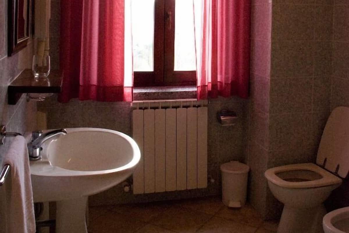 Un baño con lavamanos, inodoro y ventana con cortinas rojas.