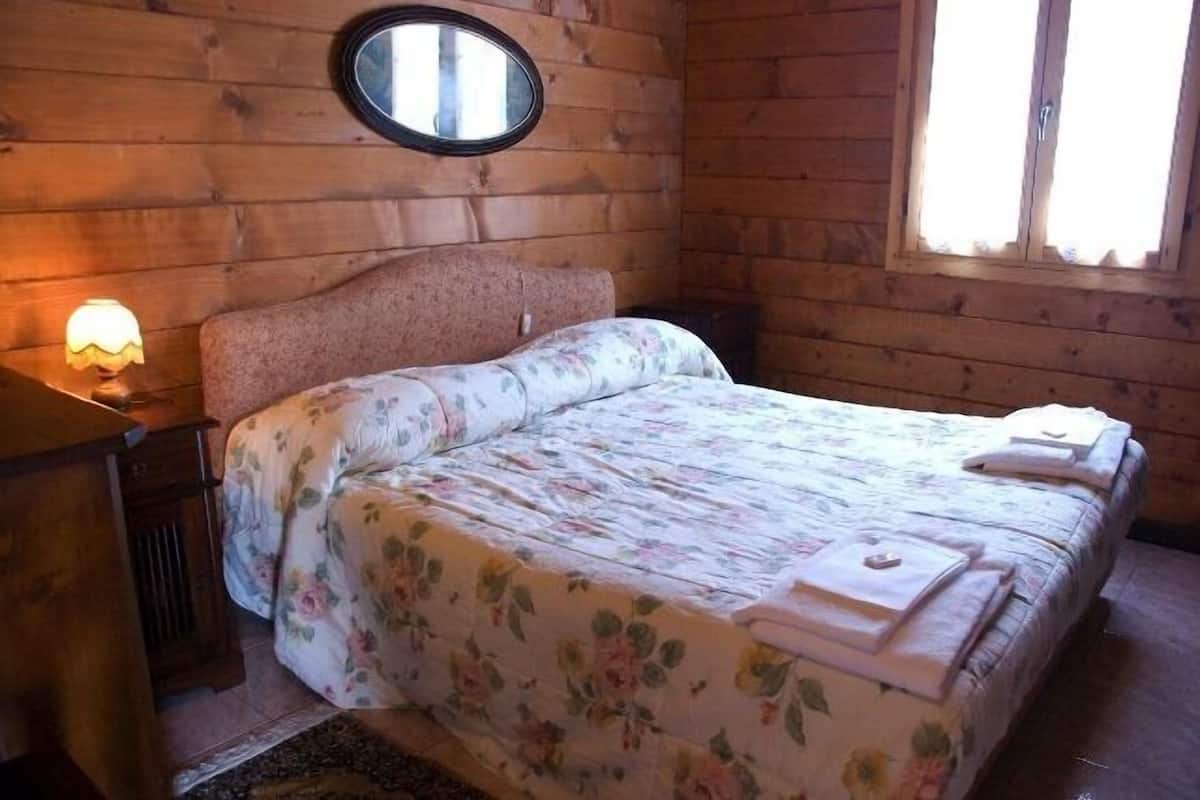 Un dormitorio de cabaña de madera con una cama, una mesita de noche, una lámpara y una ventana.