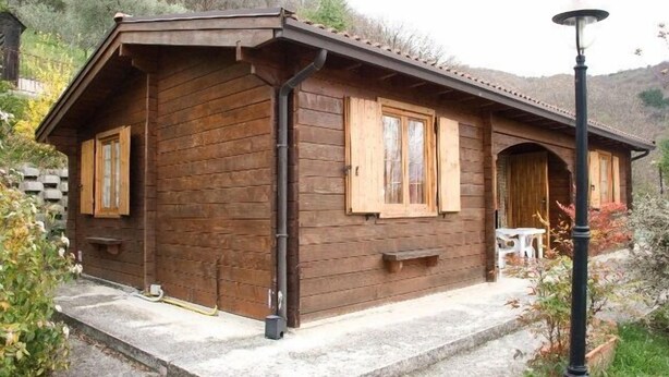 A wooden cabin with a sloped roof, a porch with a bench, and a small table. - Agriturismo Le Francesche (Nocera Umbra)