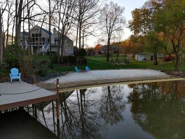 A lakeside property with a dock, a sandy area, and a house in the background.
