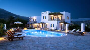 Un hotel moderno con piscina, sillones de descanso y montañas al fondo.