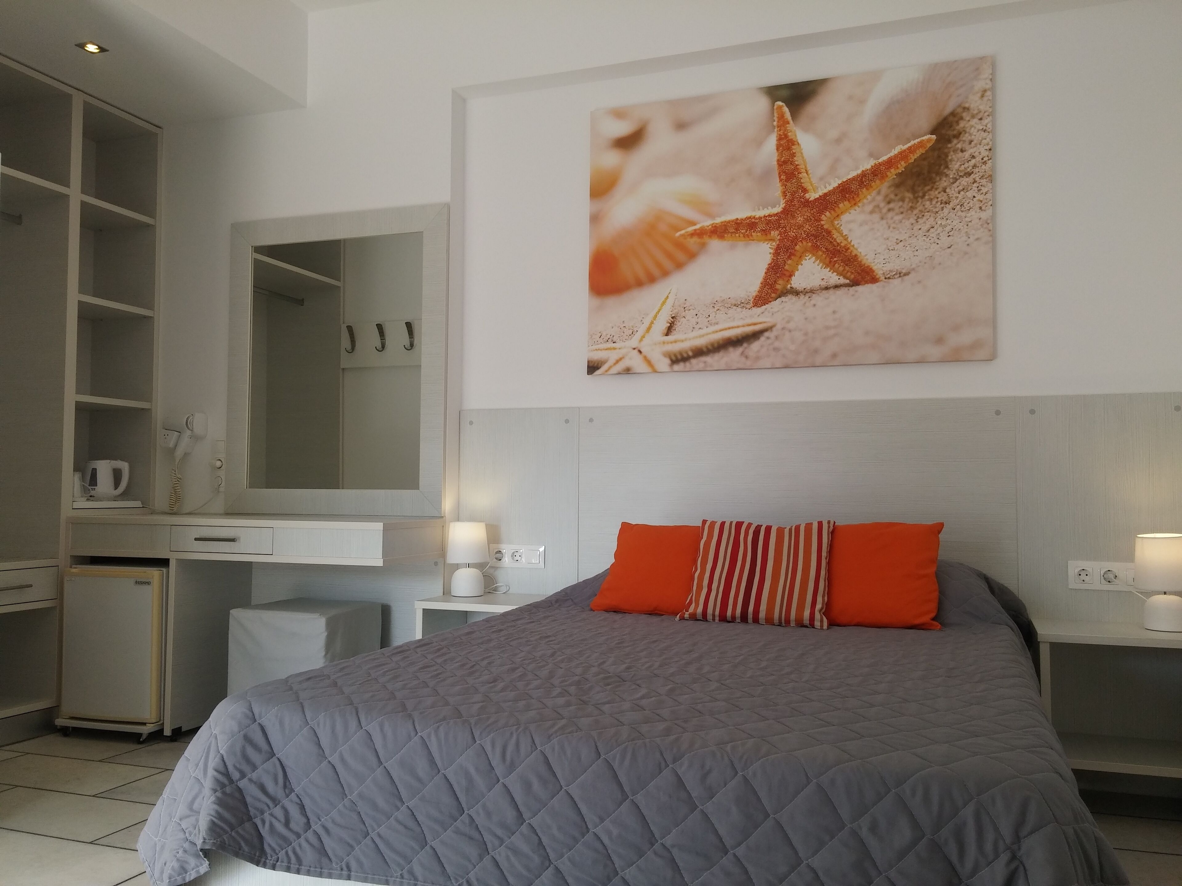 Un dormitorio con cama, escritorio, espejo y un cuadro en la pared de una estrella de mar.