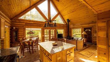 A spacious log cabin interior with a large kitchen area, dining space, and a cozy living area.