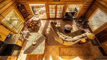 A log cabin interior with a dining area, a sofa, a fireplace, and a kitchen.