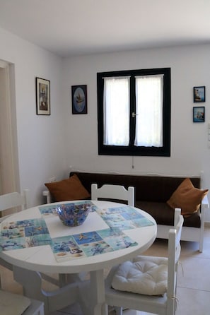 Una habitación con una mesa redonda, sillas blancas, un sofá marrón y una ventana con cortinas.