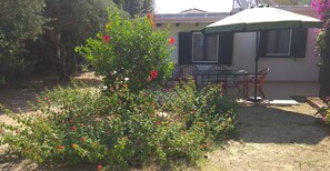 A garden with flowering plants and a patio area with a table and chairs. - Guest House  steps from ocean... (Chersonissos)