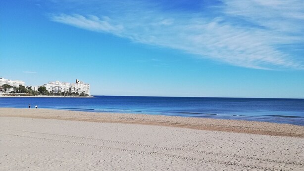 Een strand met een heldere lucht, een zandstrand en een gebouw op de achtergrond.