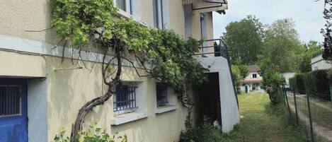 Un edificio con techo inclinado, puerta azul y un pequeño jardín con césped y plantas.