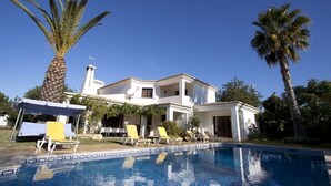 Una casa de dos pisos con piscina, palmeras y un área de estar techada.