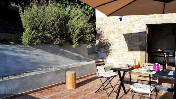 Un patio al aire libre con un muro de piedra, una mesa de madera con sillas y un paraguas grande que da sombra.