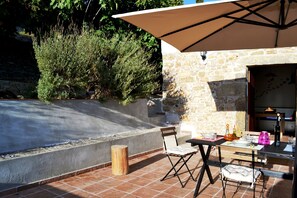 An outdoor patio with a stone wall, a wooden table with chairs, and a large umbrella providing shade. - the house in the vineyard, a refined country house (Erice)
