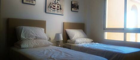 Habitación de hotel con dos camas, cada una con cabecero y almohadas, una mesita de noche con lámpara y una obra de arte en la pared.