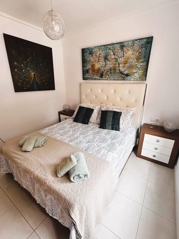 A bedroom with a tufted headboard, a large abstract painting, and a bedside table with a lamp.