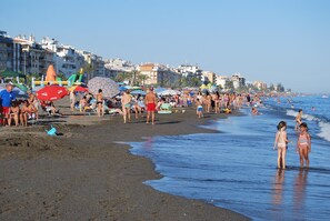 Une plage bondée, avec des gens, des parasols et des chaises de plage.