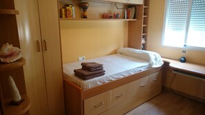 Une chambre à coucher de taille modeste, comprenant un lit simple, une armoire en bois et une étagère ornée d’objets décoratifs.