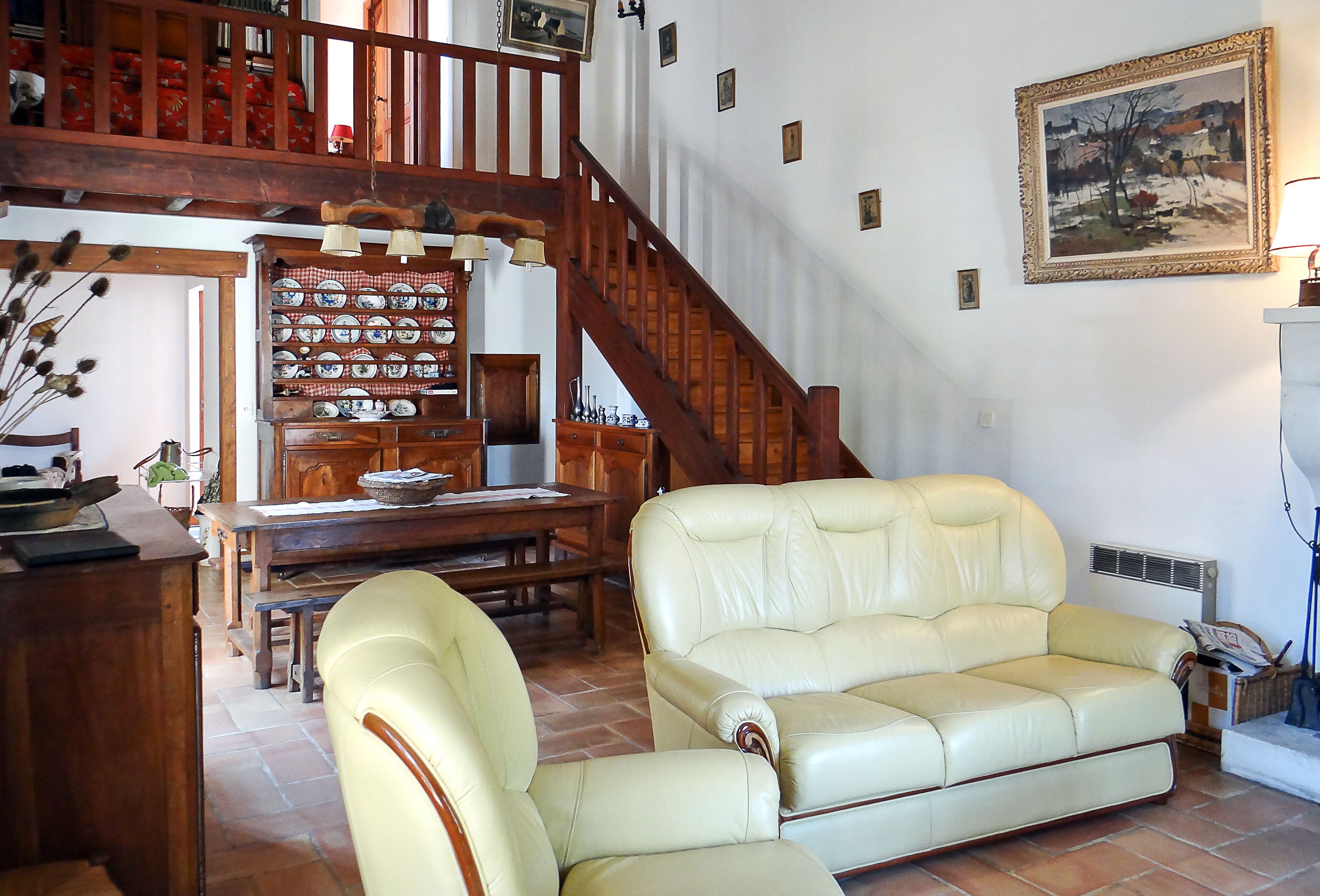 A living room with a sofa, a dining table with chairs, a staircase, and a wall with framed pictures.