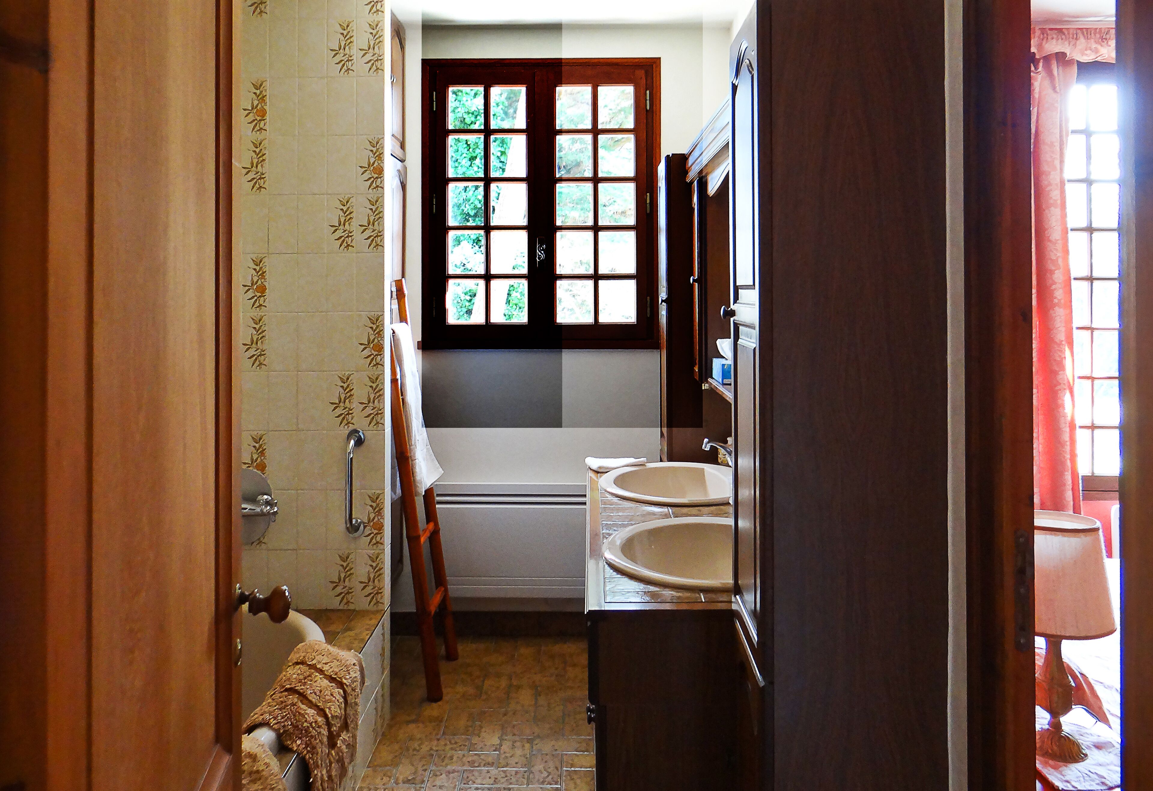 A bathroom with a bathtub, two sinks, and a window with a view of greenery.