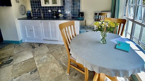 Een eetruimte met een ronde tafel, stoelen en uitzicht op de keuken.