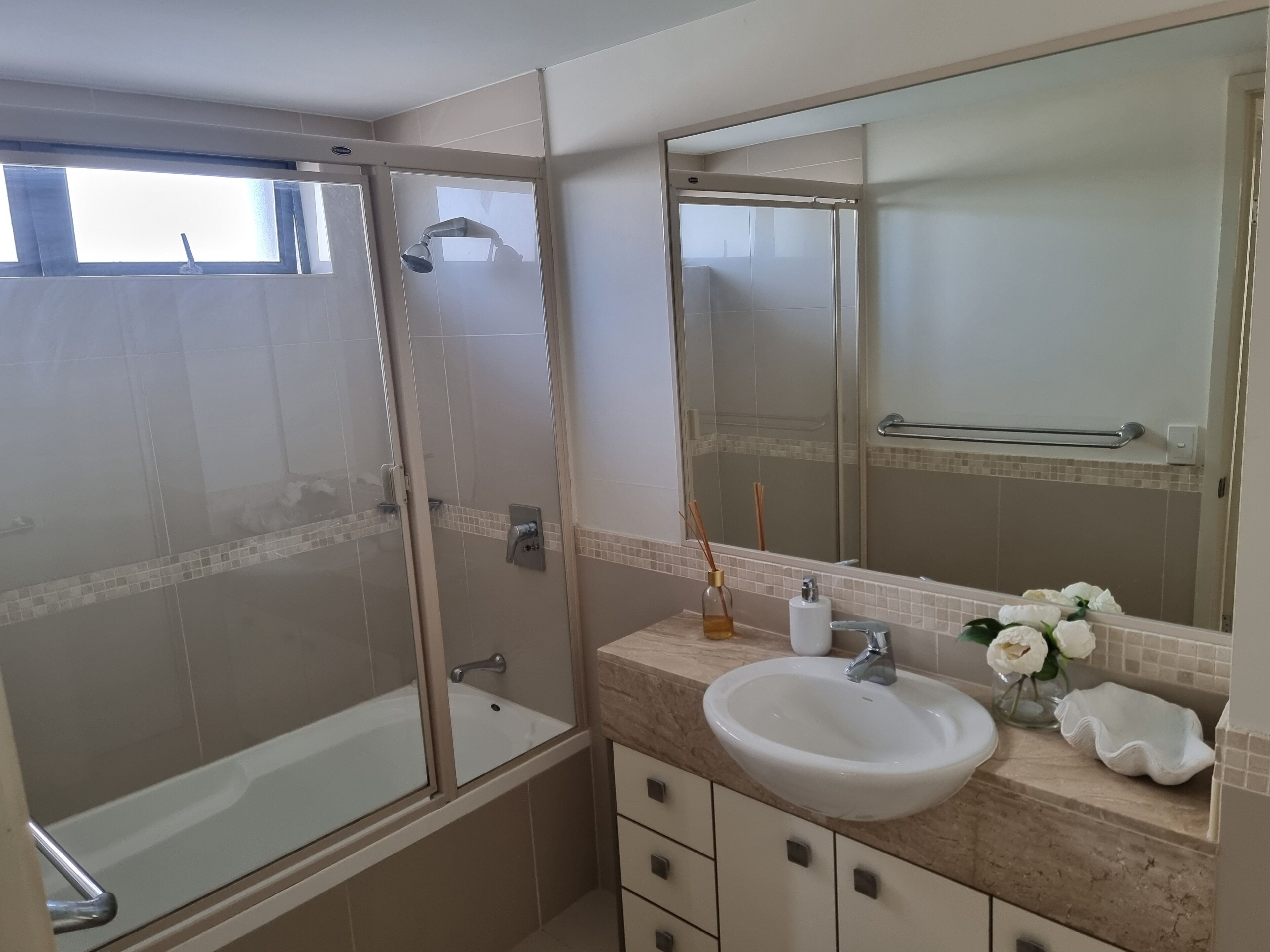 A modern bathroom with a glass-enclosed shower, a white sink, and a large mirror.