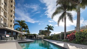 A swimming pool with a depth marker, surrounded by palm trees and a building with balconies. - The Waterford Prestige Apartments (Caloundra)