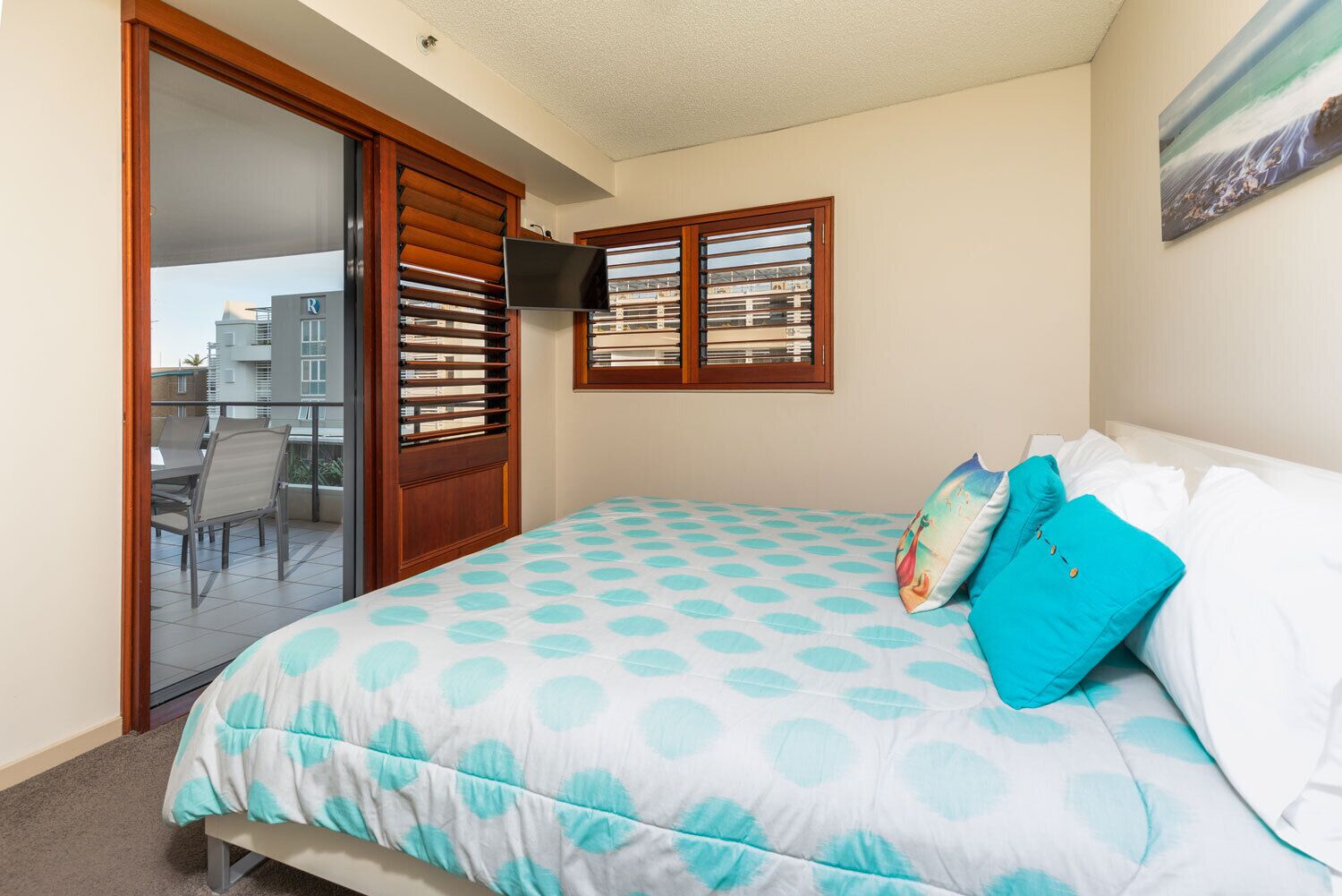 Ein Schlafzimmer mit Bett, Fernseher, Balkon mit Stühlen und Blick auf Gebäude.
