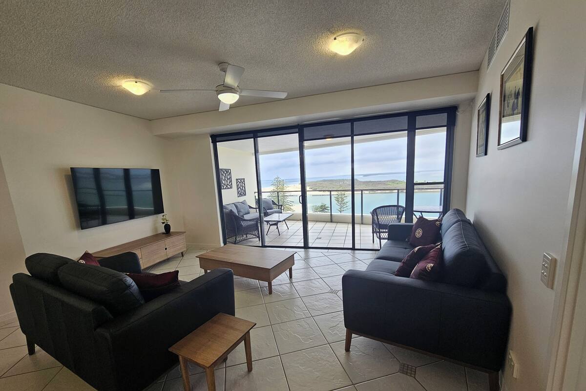 Una sala de estar con televisor, sofás, una mesa de centro y un balcón con vistas.