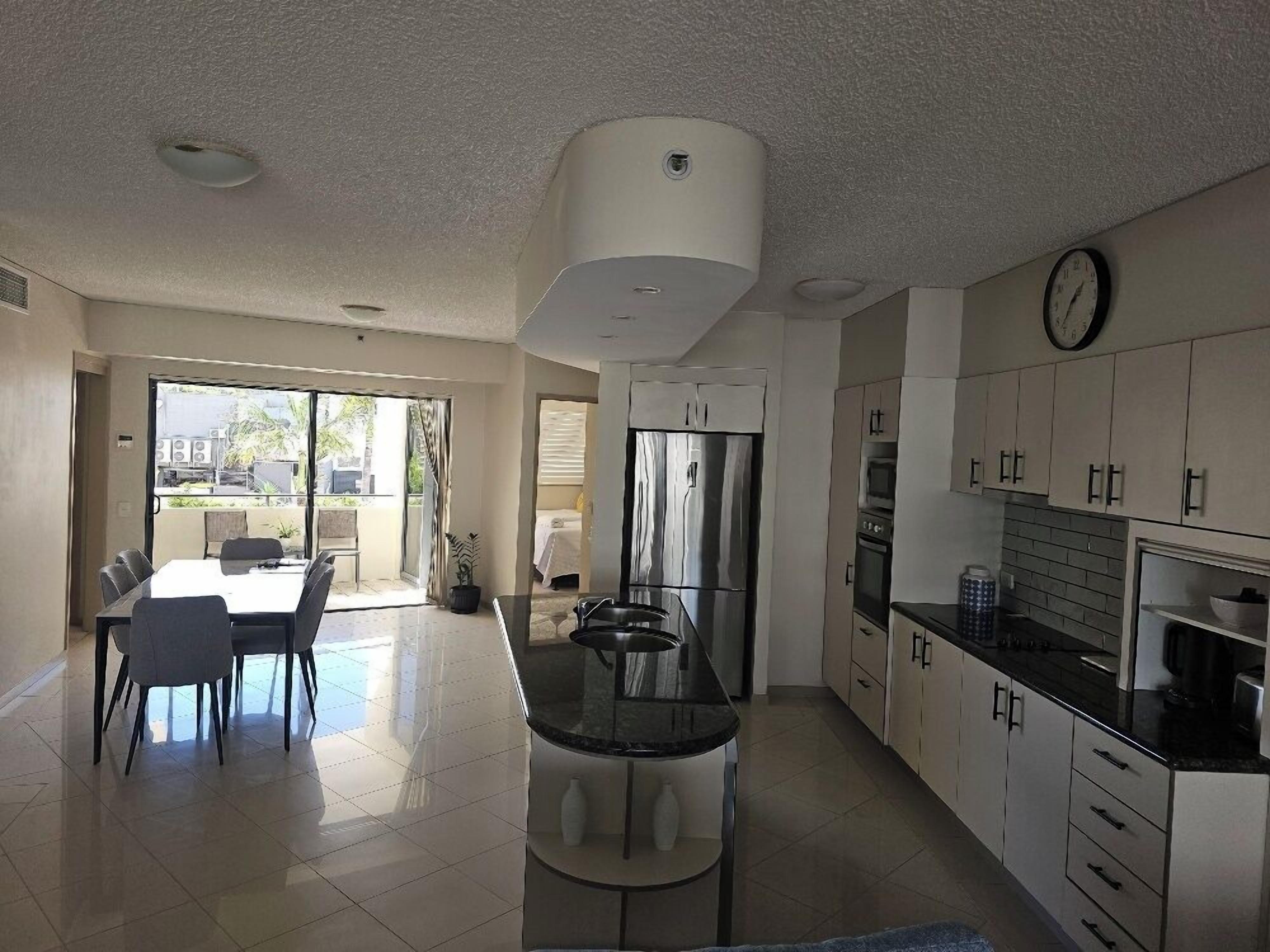 A modern kitchen with a central island, a dining area with chairs, and a large window providing natural light.