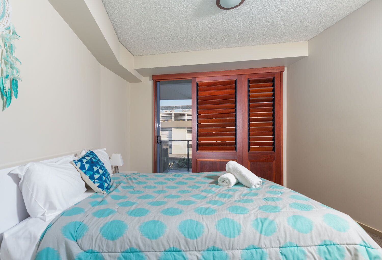 A hotel room with a bed, a nightstand, a window with blinds, and a view of the outside.