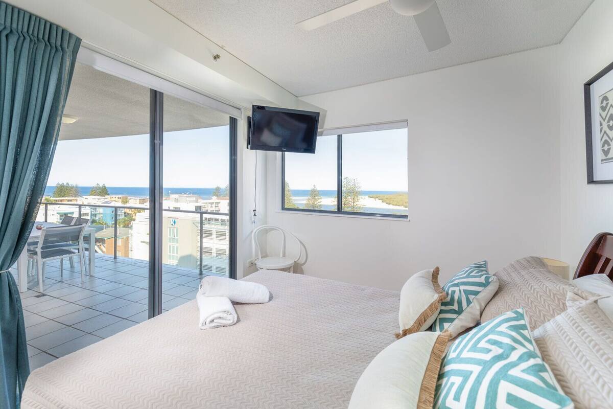 Habitación de hotel con cama, televisión, balcón con vistas al mar y una silla.