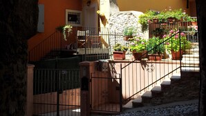 A courtyard with a stone staircase leading to a building with orange walls and a balcony. - Great Price... Romantic Apartment Near Beaches and Nightlife (Malcesine)
