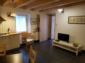 A kitchen with a dining area, a TV, and a wicker chair.