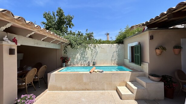 A swimming pool with steps leading into it, surrounded by a patio area with chairs and potted plants. - Maria Ca Sa Padrina (Maria de la Salut)