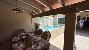 A dining area with a pool view, featuring a table set for two, wicker chairs, and a hanging light fixture. - Maria Ca Sa Padrina (Maria de la Salut)