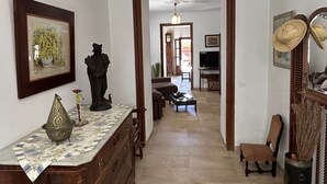 A hallway with a wooden dresser, a framed picture, a statue, and a television in the background. - Maria Ca Sa Padrina (Maria de la Salut)