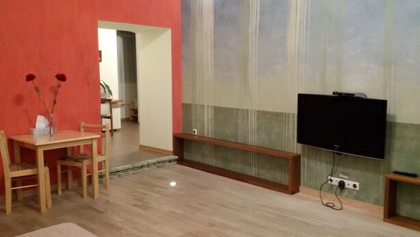 Un salon doté d’un plancher en bois, d’un téléviseur fixé au mur et d’un coin repas avec une table et des chaises.