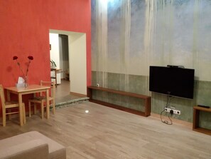 Un salon doté d’un plancher en bois, d’un téléviseur fixé au mur et d’un coin repas avec une table et des chaises.