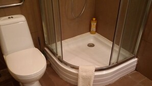 Une salle de bain avec des toilettes, une douche à parois de verre et un tapis de bain jaune.