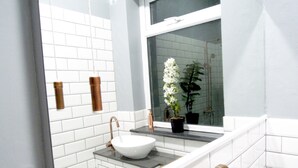 A bathroom with a white sink, a potted plant, and a window.