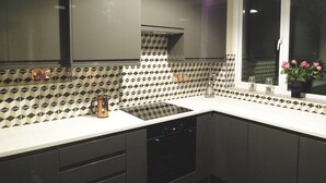 A modern kitchen with black cabinets, a white countertop, and a patterned backsplash.