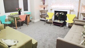 A living room with a fireplace, a dining table, and colorful chairs.