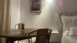 A room with a dining table, chairs, a bed with a striped curtain, and a framed picture on the wall. - Garden in town (Lyon)