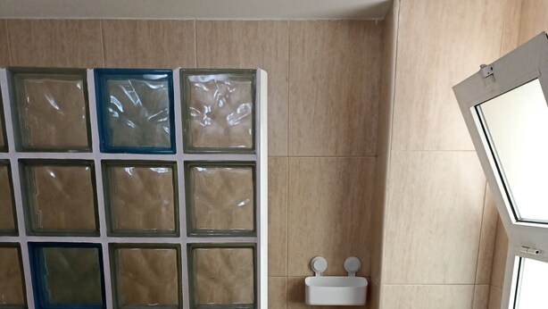 Een badkamer met een betegelde douche, een witte wastafel en een raam.